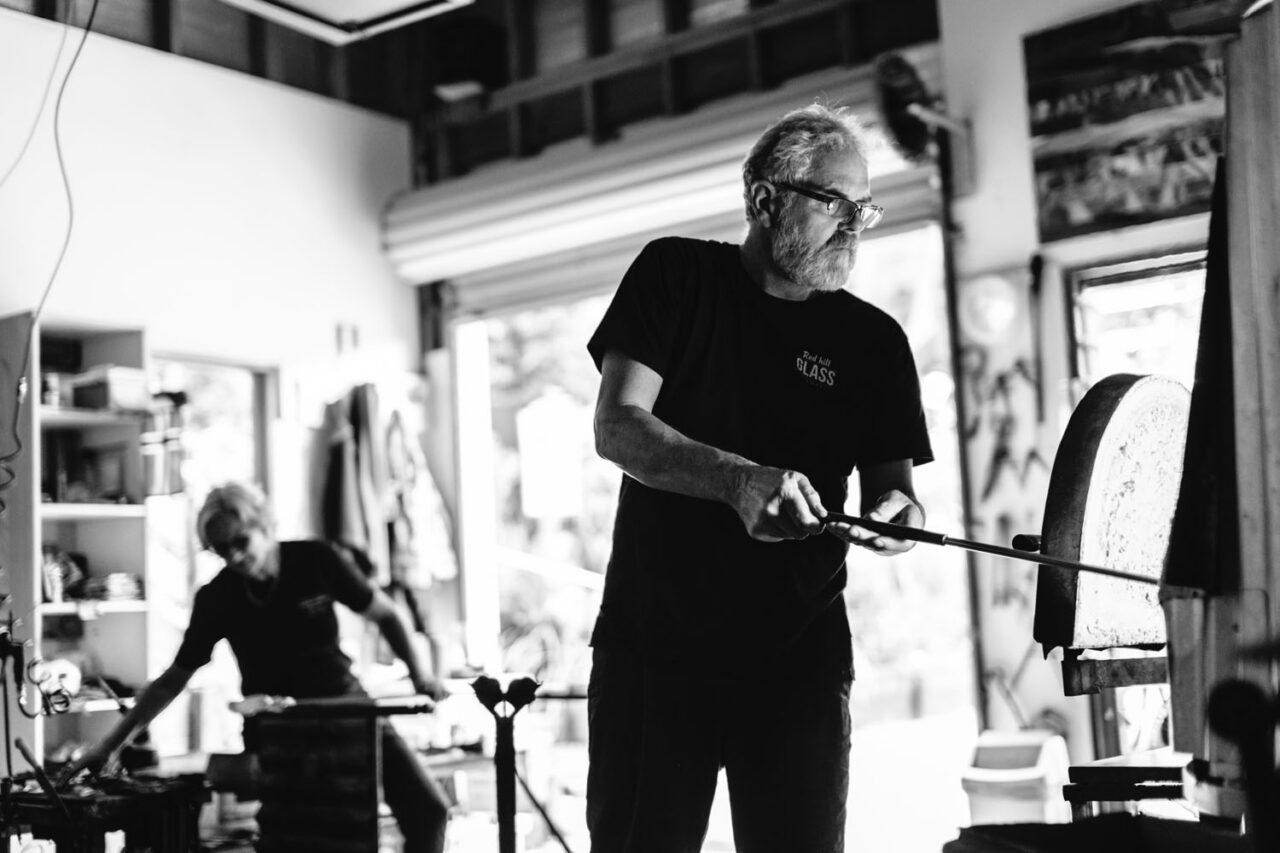 Glass artist shaping molten glass in studio, black and white documentary brand photography.