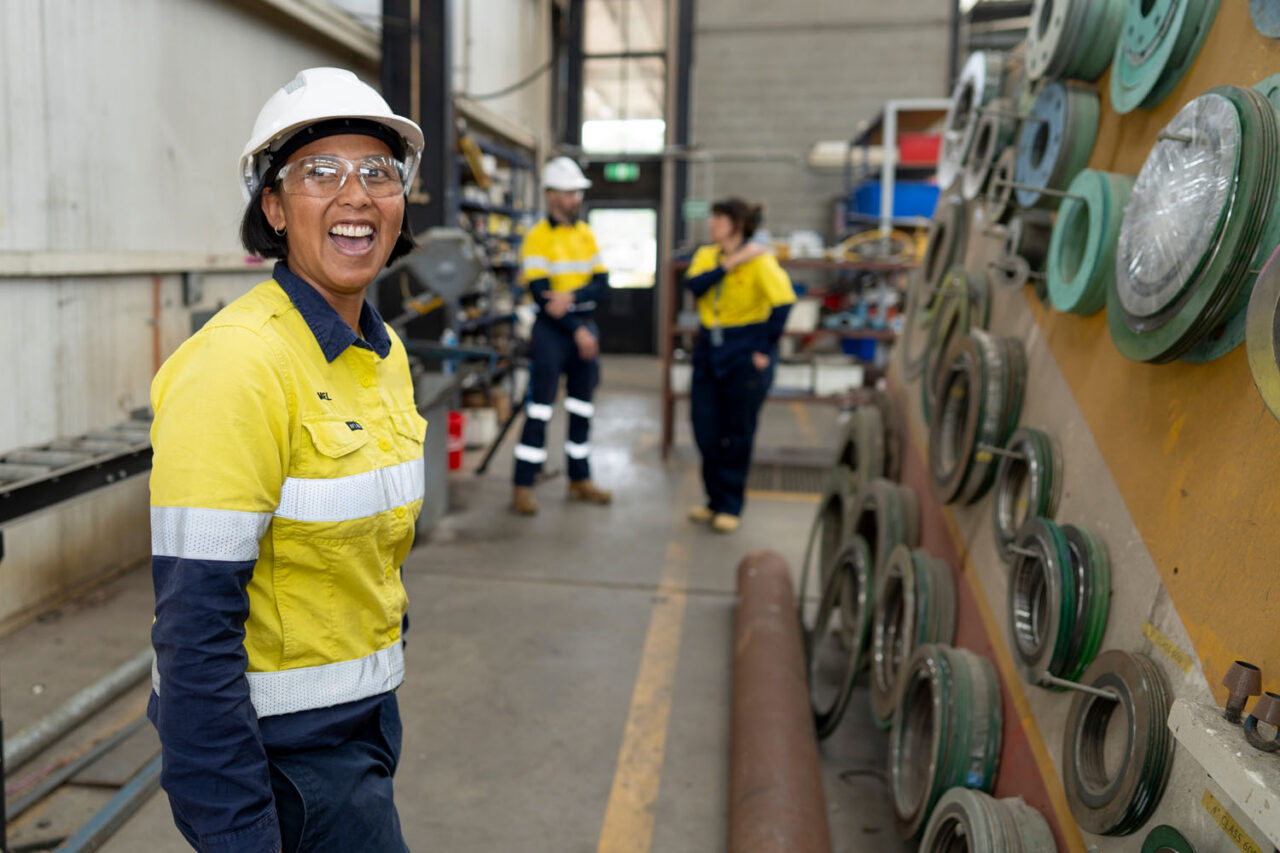 Worker in high-vis uniform smiling inside an industrial workshop, lifestyle brand photography for a Dandenong-based organisation.