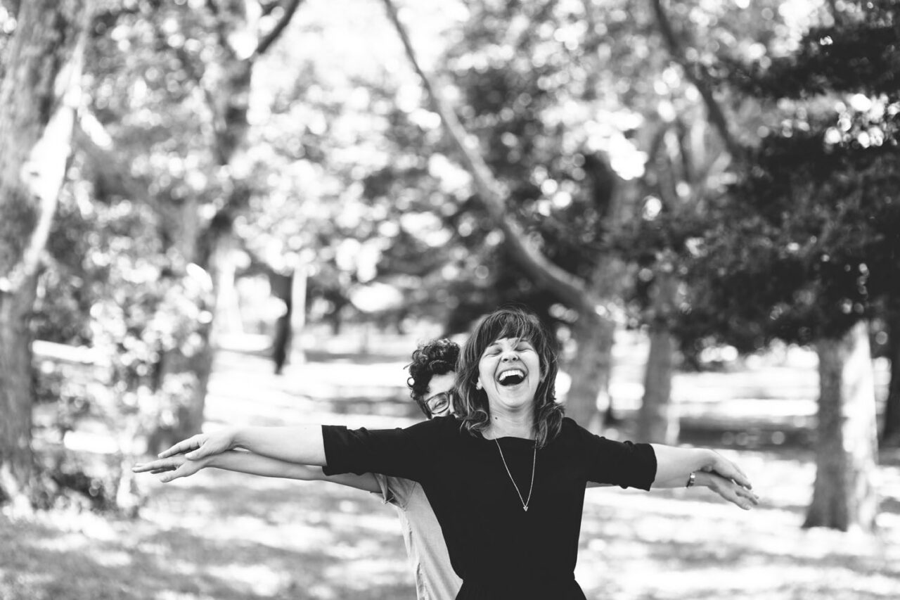 Queer couple laughing together during a relaxed, documentary-style wedding moment in nature.