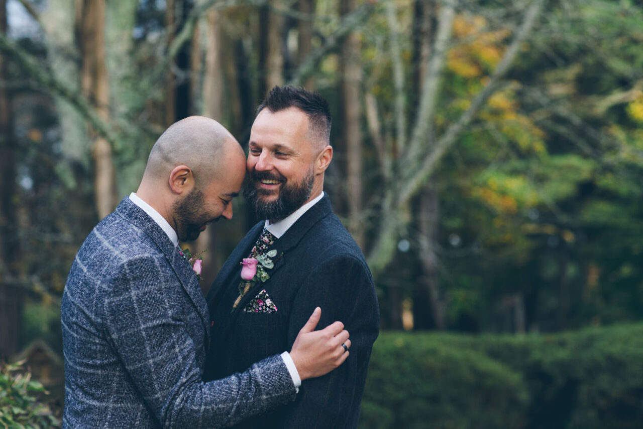 Two grooms sharing a quiet, emotional moment together during a forest wedding ceremony.