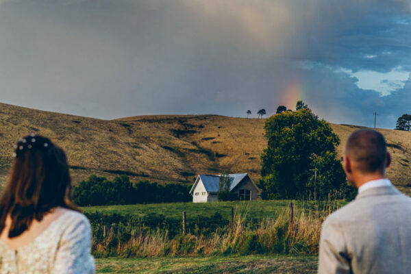 wedding couple overlooking a rural landscape with a rainbow in the sky, candid documentary wedding photography by LJM Photography