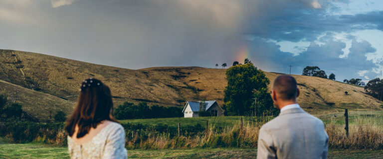 wedding couple overlooking a rural landscape with a rainbow in the sky, candid documentary wedding photography by LJM Photography