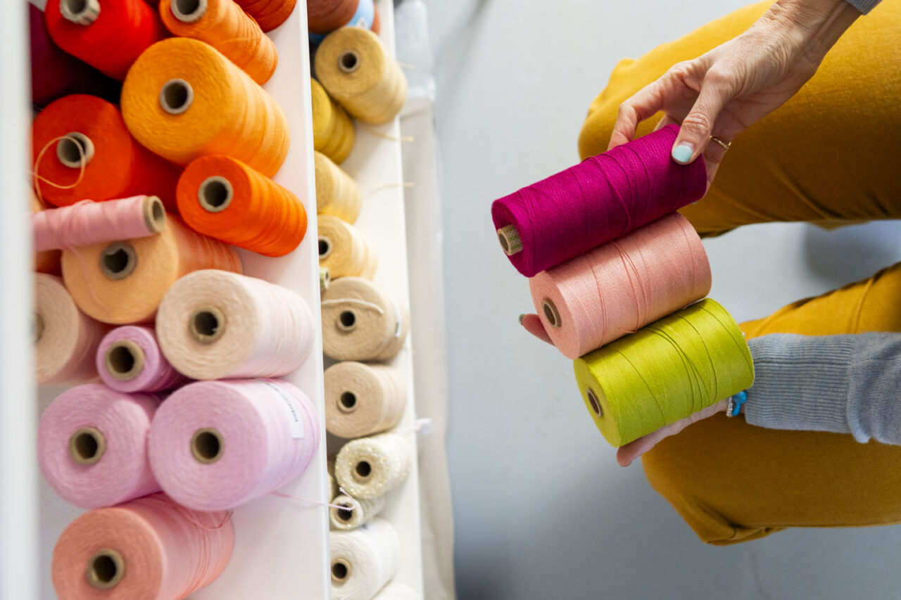 Hands selecting bright thread spools in creative studio, behind the scenes brand photography documenting artistic process in Melbourne