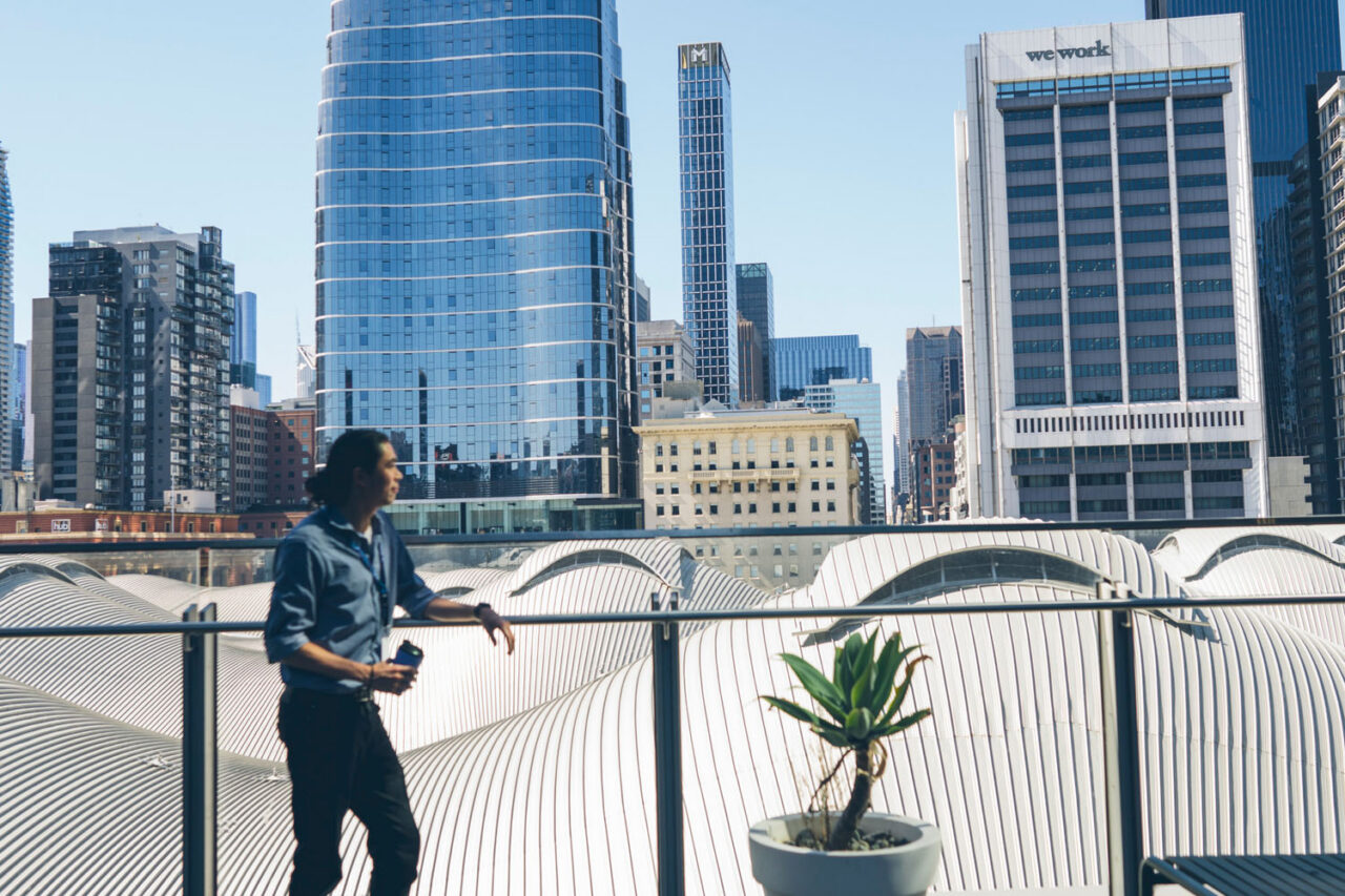Professional standing on a balcony overlooking Melbourne CBD skyline, corporate lifestyle brand photography.