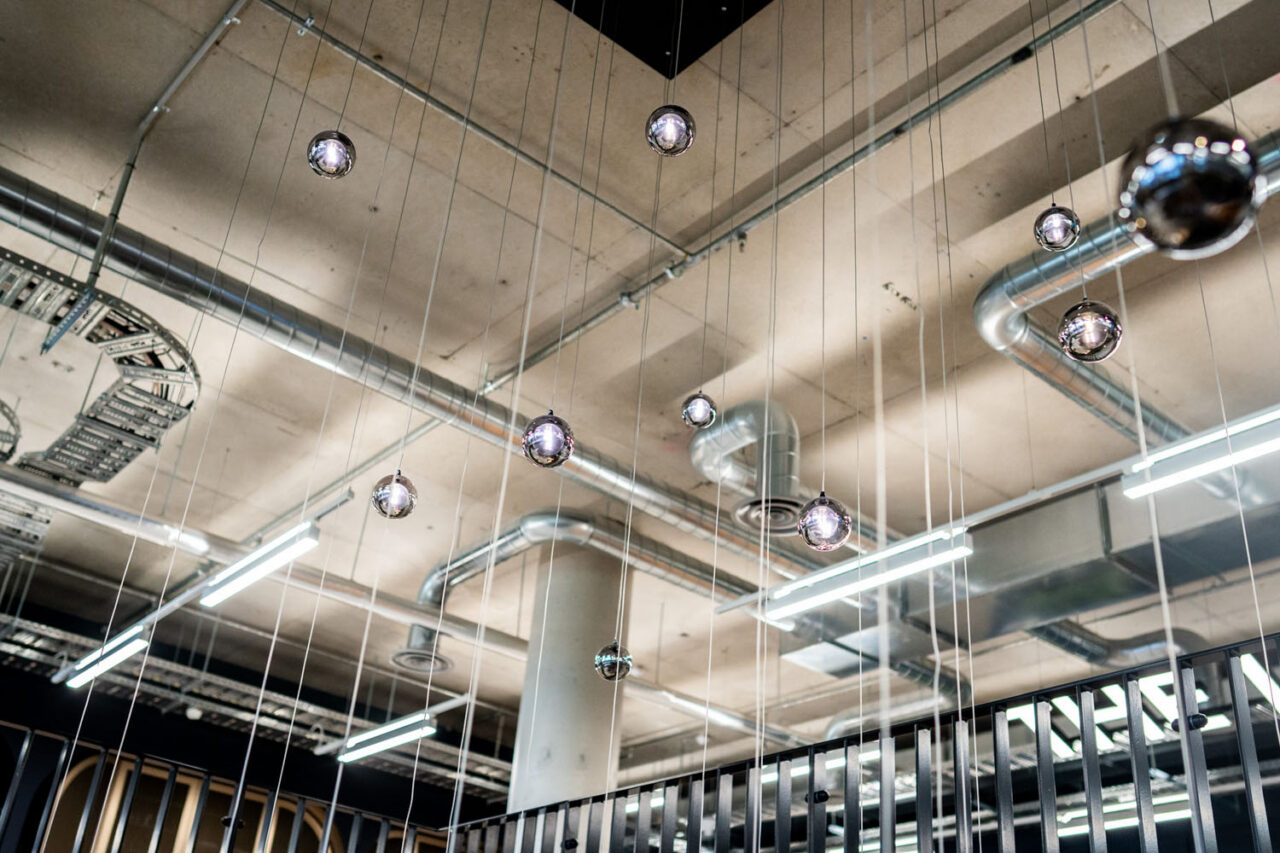 Modern coworking space ceiling with hanging pendant lights and exposed ducting