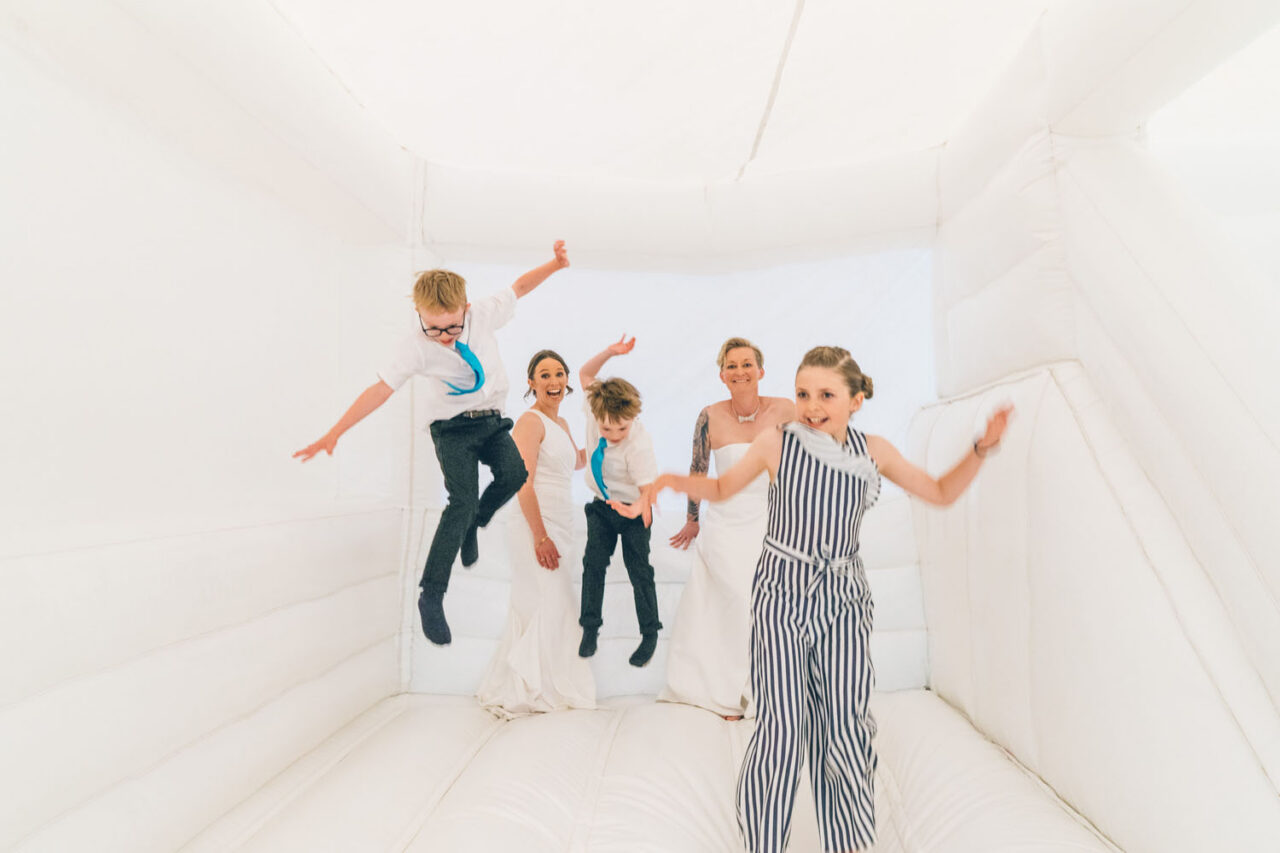Queer family jumping together in an inflatable during the wedding, joyful candid moment