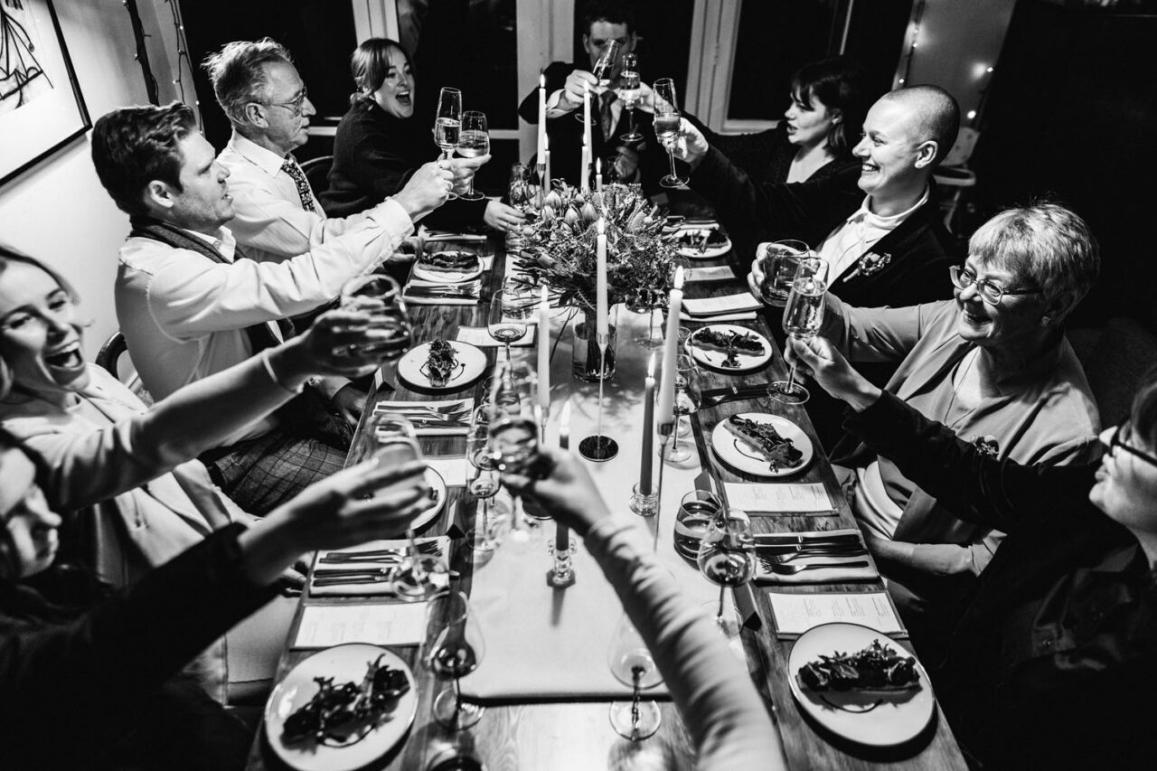 Guests raising glasses at a queer wedding dinner, emotional documentary style moment