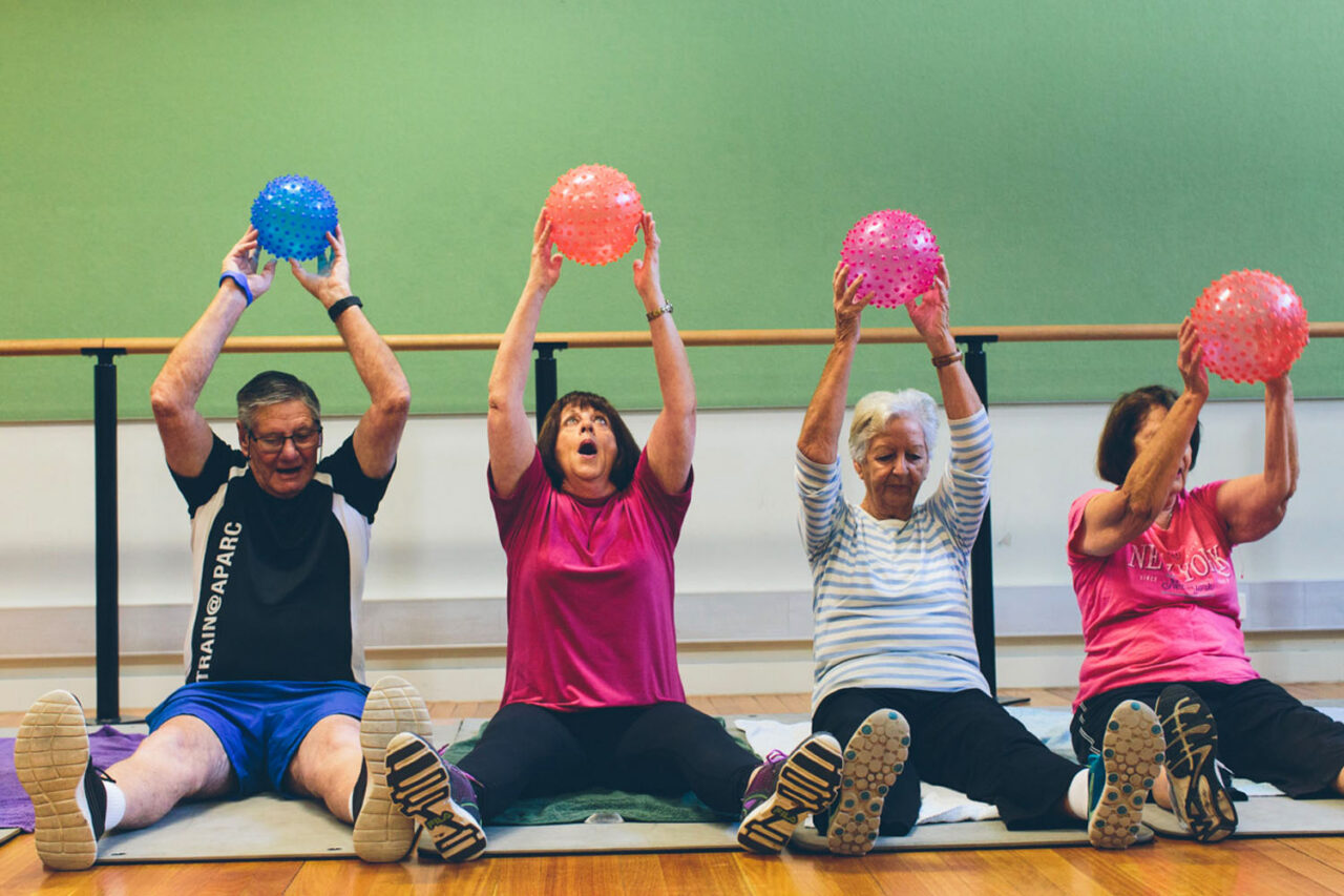 Older adults lifting textured exercise balls during a YMCA group fitness class