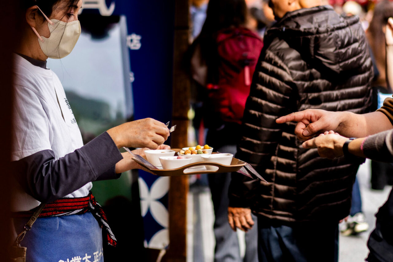 Street food vendor handing samples to visitors in Asakusa, Tokyo