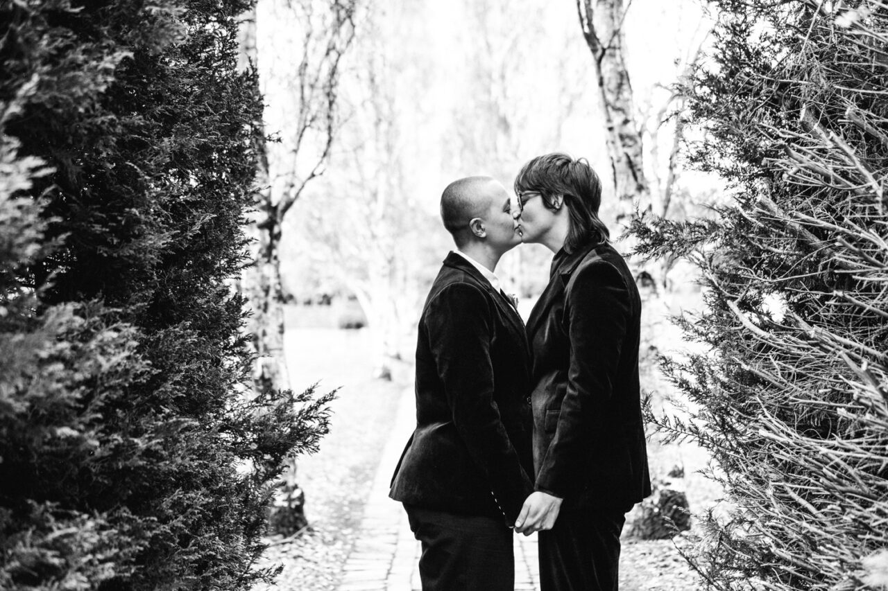 Black and white portrait of Naomi and Bec kissing between trees at their Daylesford wedding.