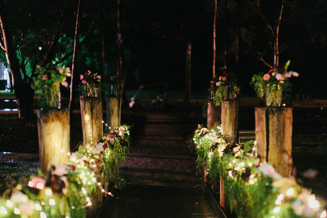 Outdoor wedding ceremony aisle decorated with flowers and warm lighting by Botanics of Melbourne.