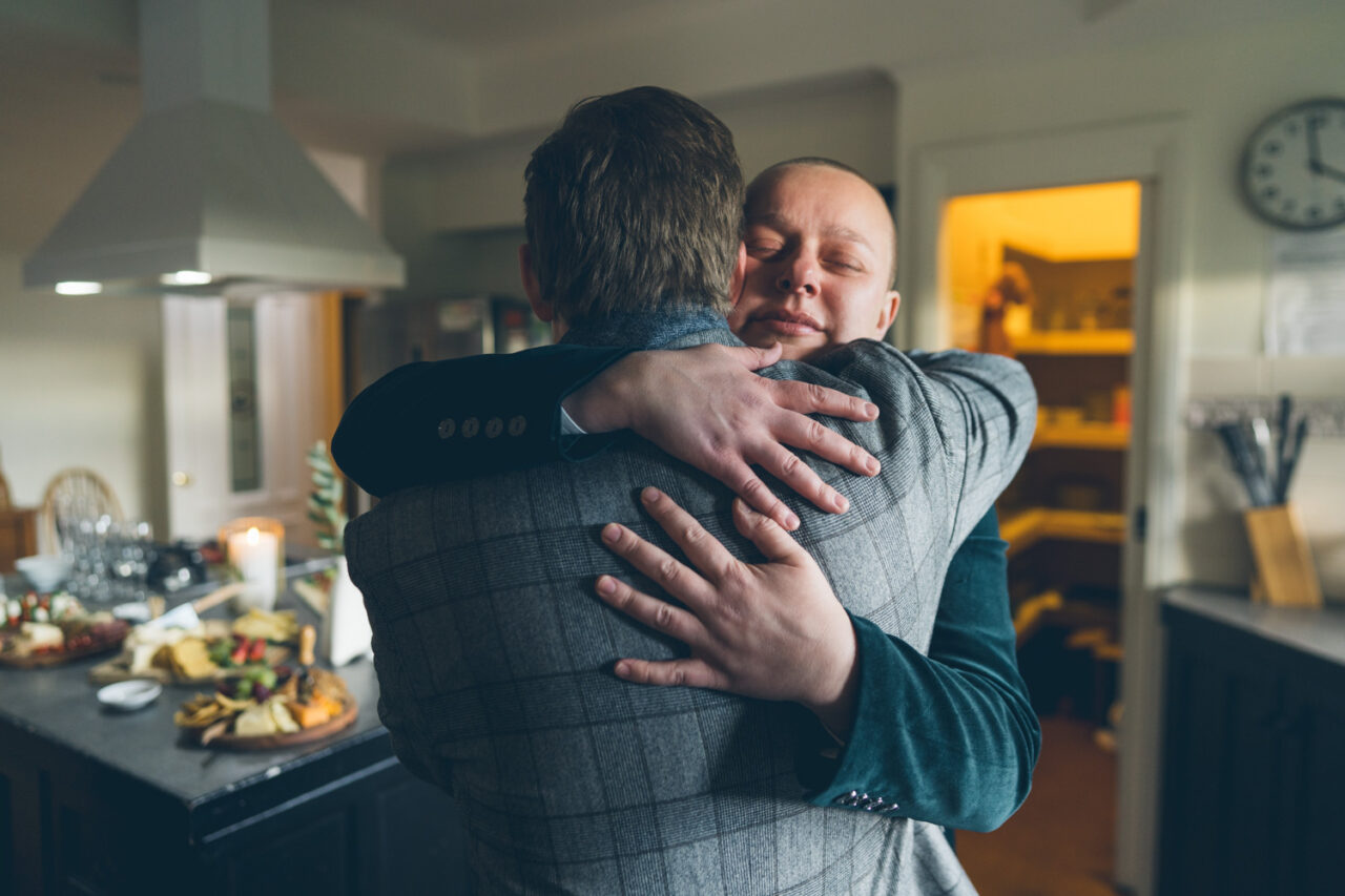 Emotional hug between Naomi and a family member in a kitchen during wedding preparations.