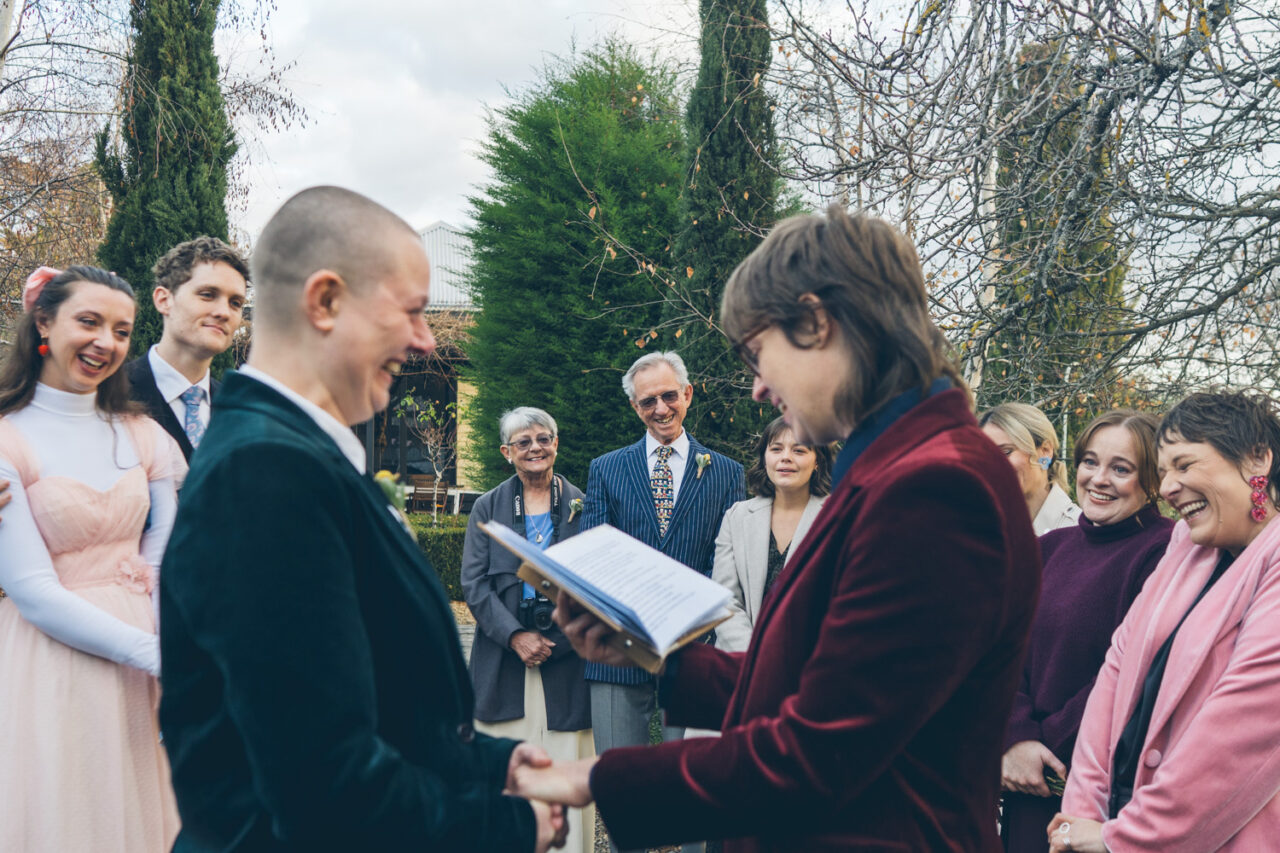 Naomi and Bec holding hands while reading vows at their Daylesford wedding ceremony.