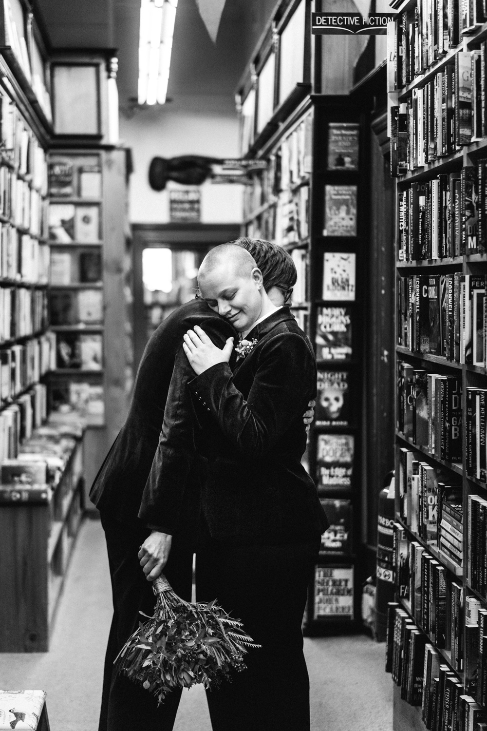 Naomi and Bec embracing between bookshelves in a Daylesford bookshop on their wedding day.