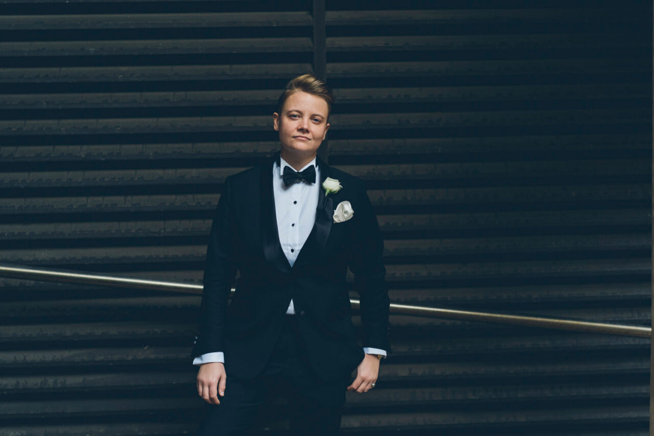Person wearing a tailored black women’s wedding suit standing confidently in a modern Melbourne wedding setting.