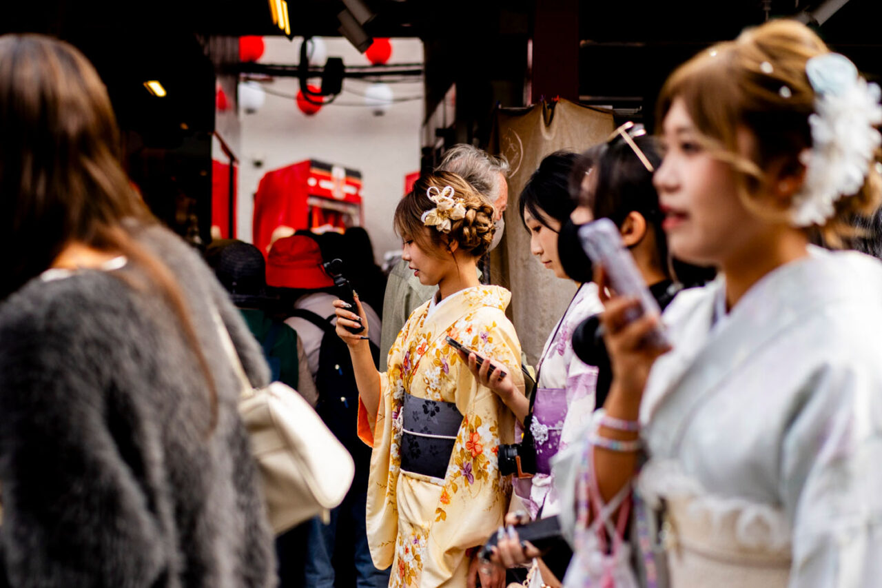 Women in colourful kimonos checking their phones in a busy Asakusa street