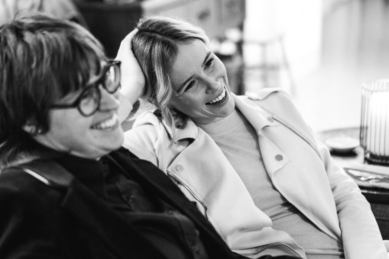 Two guests laughing together on a sofa during a relaxed queer wedding reception in Daylesford.