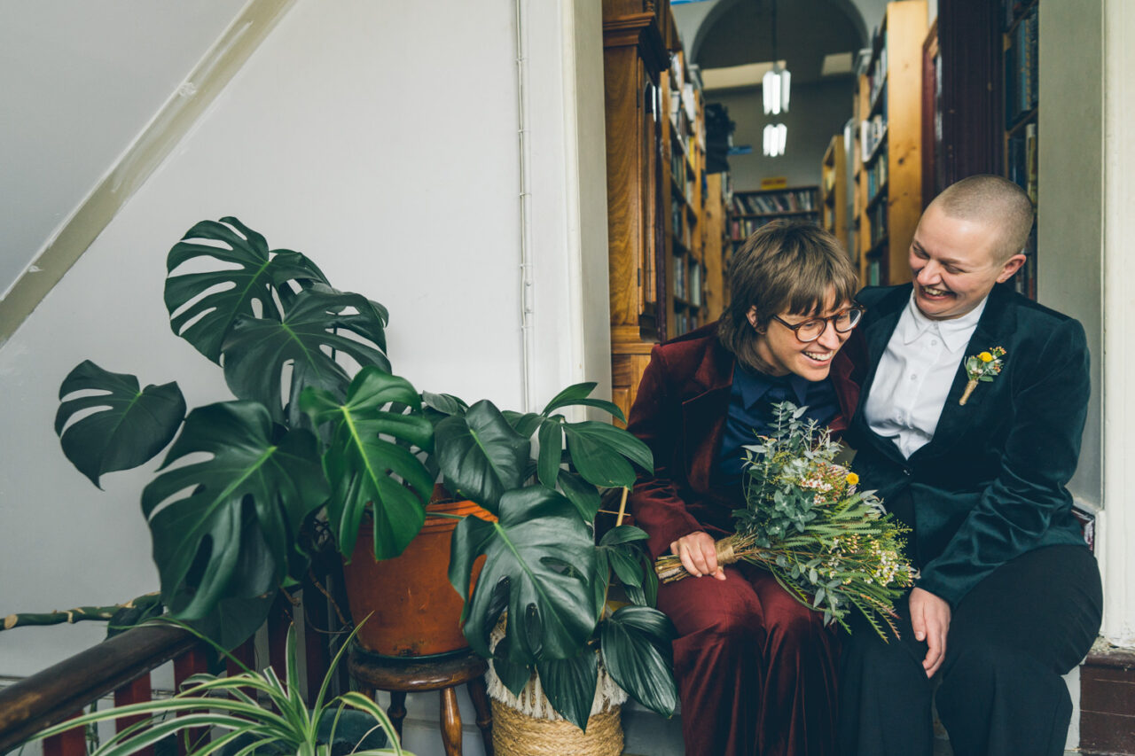 Naomi and Bec laughing together with bouquet in a bookshop doorway during their Daylesford wedding.