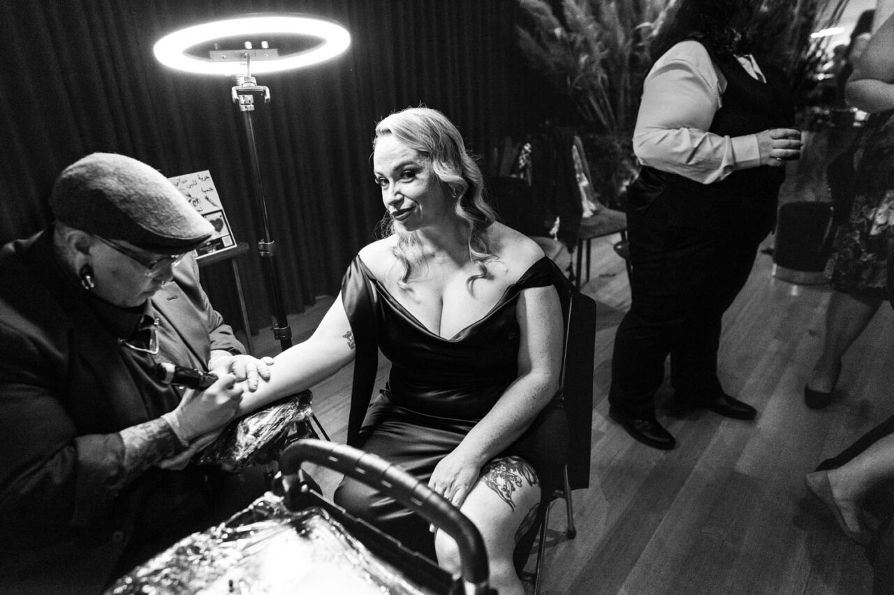 Tattoo artist Lee Stain tattooing a wedding guest at a live tattoo station during a Melbourne wedding reception.