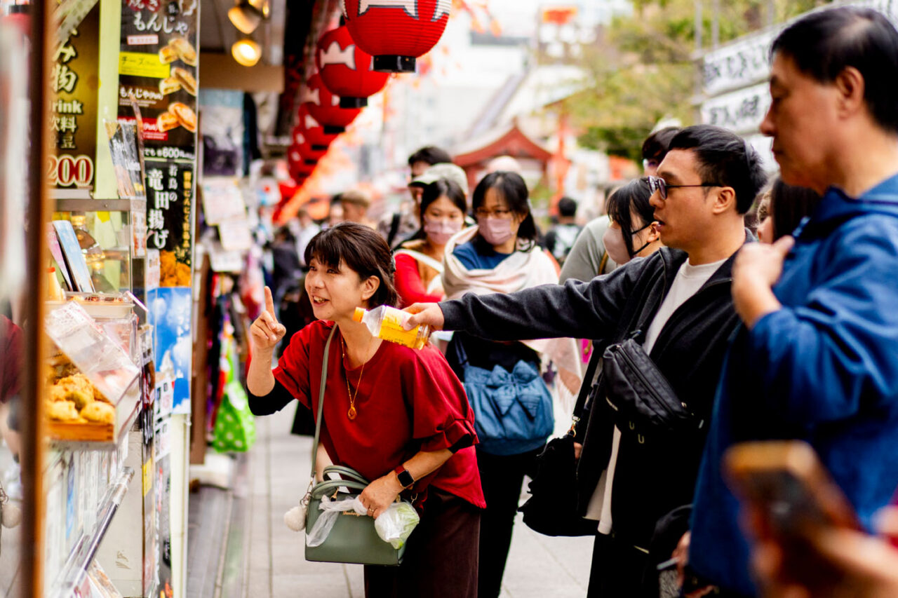 Woman pointing at food display while standing along Nakamise Street in Asakusa