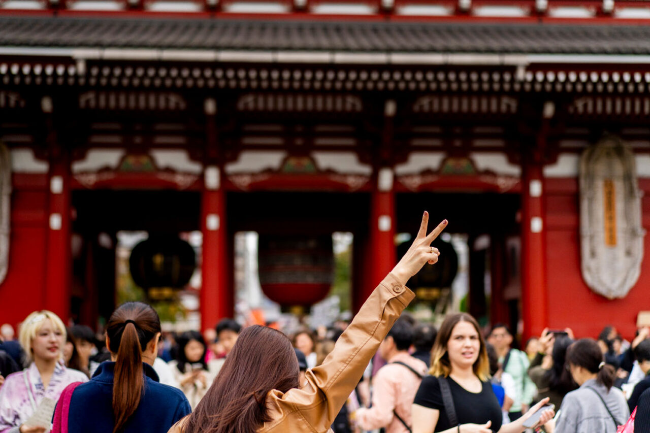 Woman raising a peace sign in front of Sensoji Temple in a crowded Asakusa street