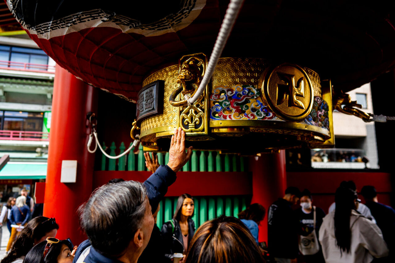 Visitors reaching up to touch a decorative lantern at Sensoji Temple in Asakusa, Tokyo