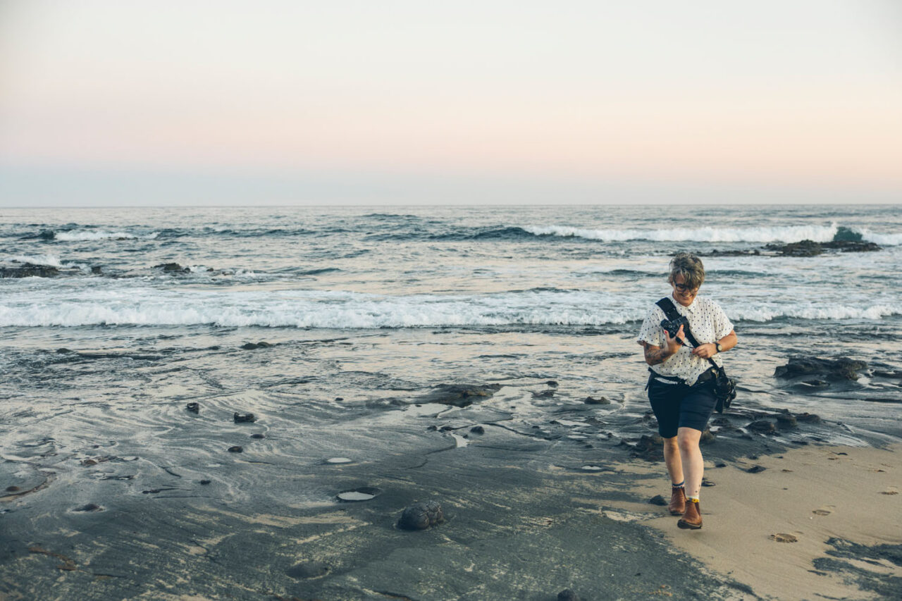 Wedding photographer walking along the Surf Coast beach with camera gear during a sunset portrait session.