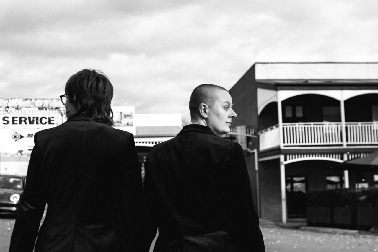 Naomi and Bec walking side by side through Daylesford in black and white on their wedding day.