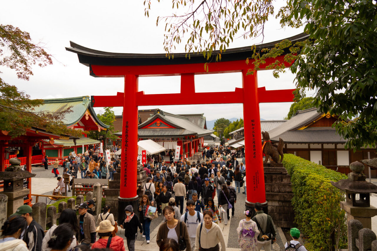 Large red torii gate at the entrance to Fushimi Inari shrine in Kyoto surrounded by a large crowd of tourists and visitors