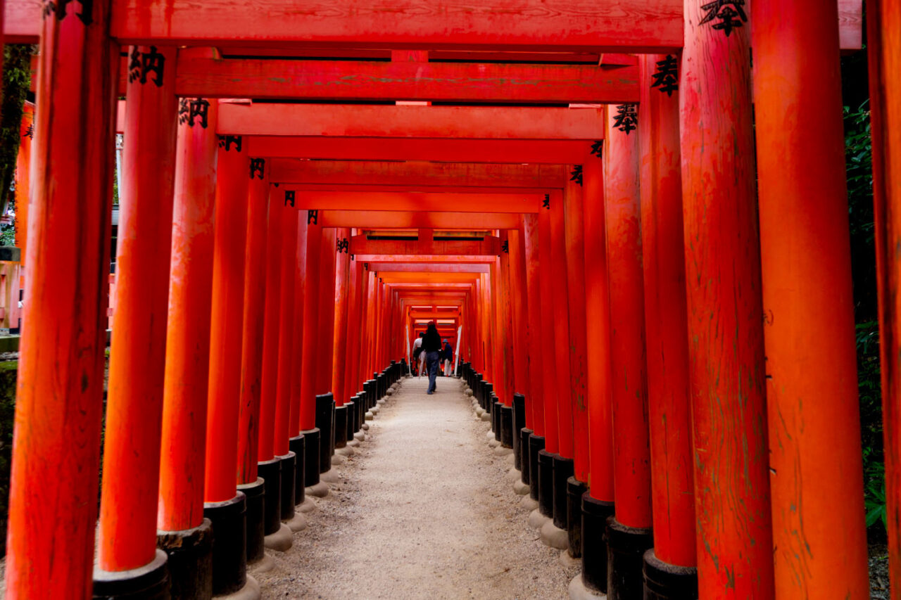 Looking down the tunnel of red torii gates at Fushimi Inari shrine in Kyoto, Japan, with a lone figure walking in the distance