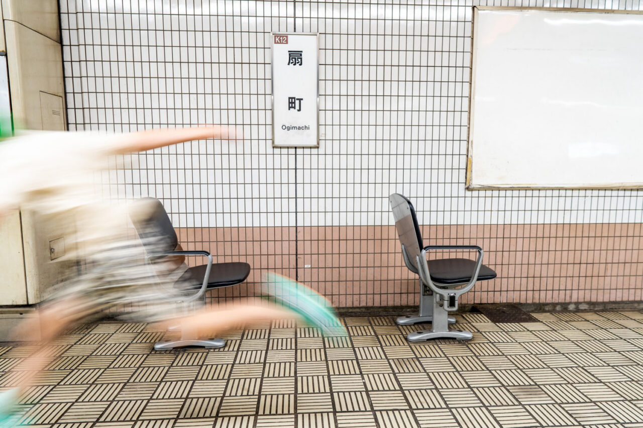 Motion blurred figure rushing past platform seats at Ogimachi subway station in Osaka Japan with station sign on tiled wall