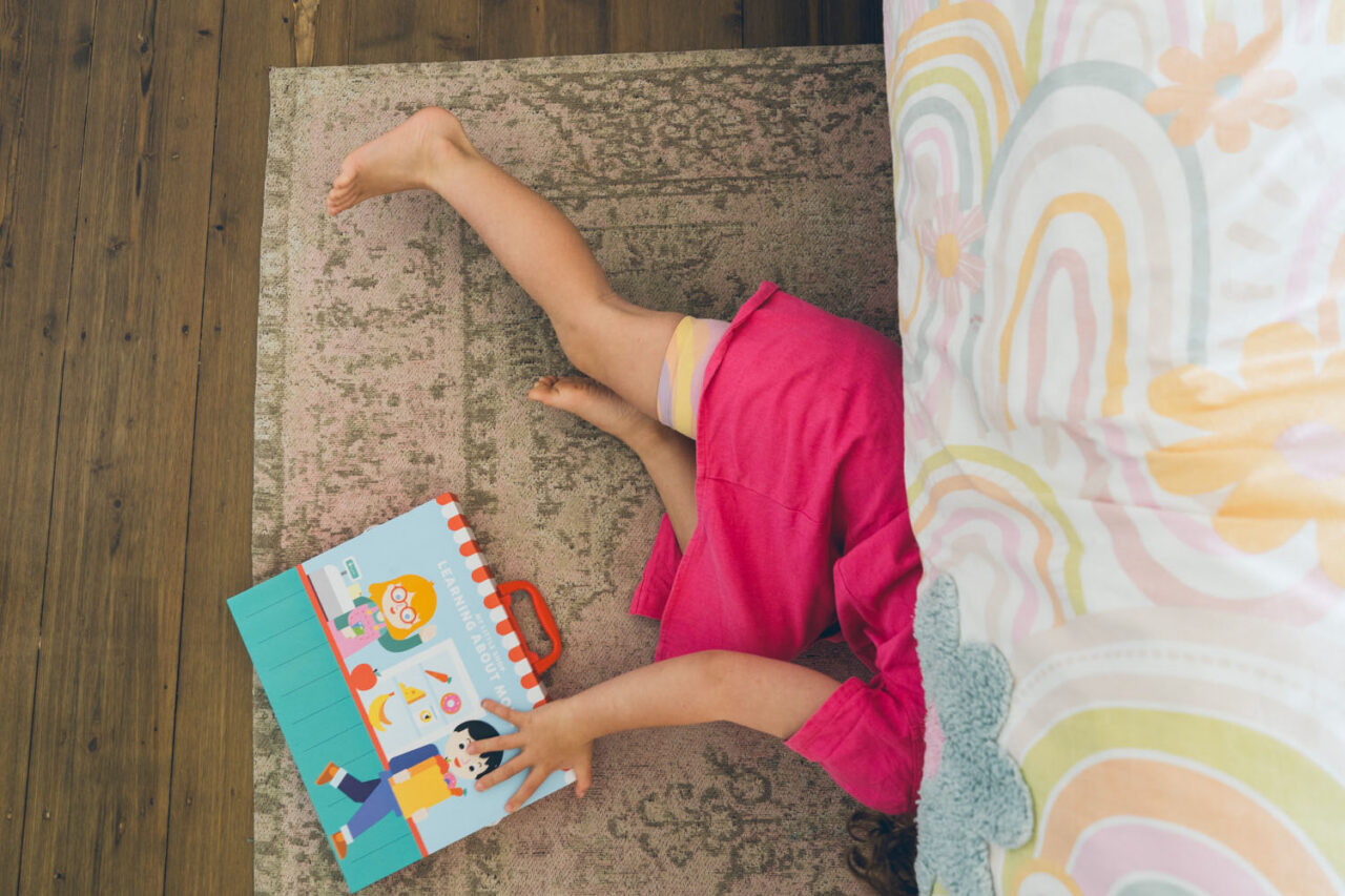 A young girl lies on her bed dressed in an Elsa costume, looking directly into the camera with wide blue eyes, captured during a documentary family photography session in Geelong 2025.