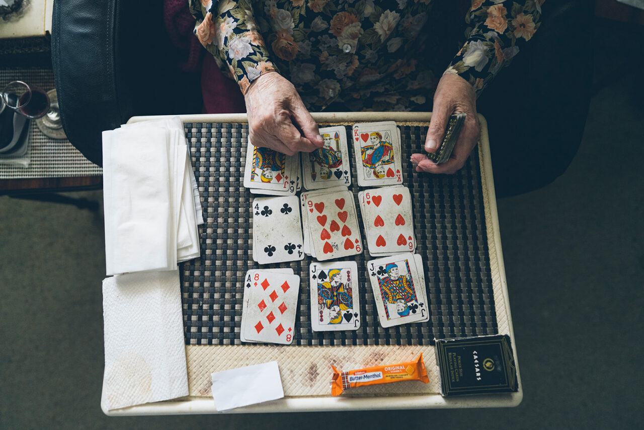 Elderly woman's hands playing cards on a tray table with butter menthol lollies nearby, documentary family home photography