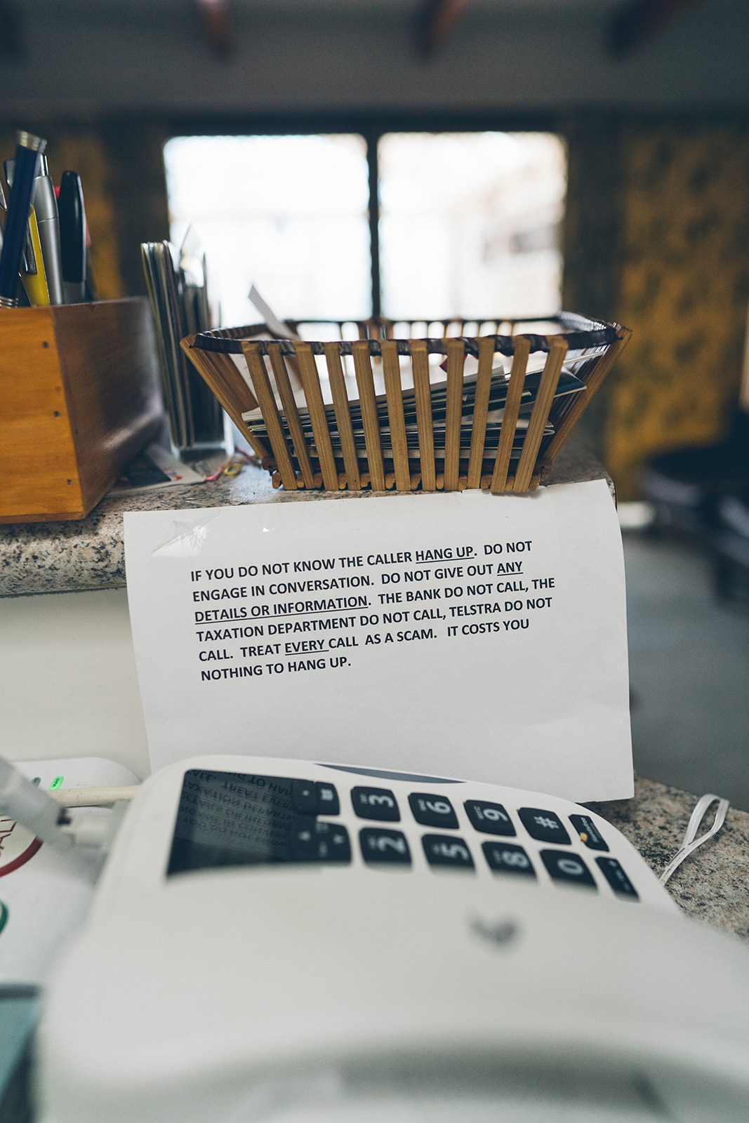Handwritten anti-scam instructions placed next to a telephone in an elderly couple's home, documentary family home photography