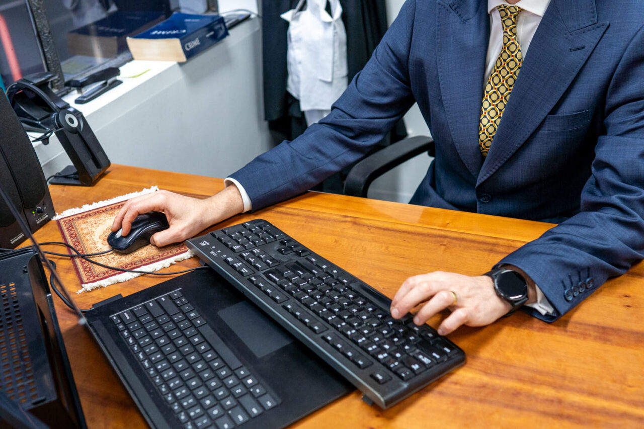 Close up detail of a barrister's hands working at a keyboard on a timber desk in a Melbourne legal office, wearing a suit with a gold patterned tie and a watch