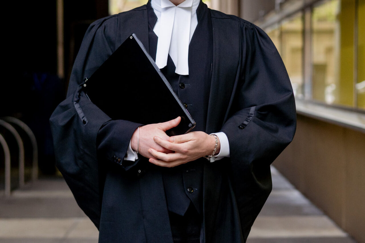 Close up detail of a barrister in traditional black robes and white jabot holding a folder outside the Melbourne Law Courts