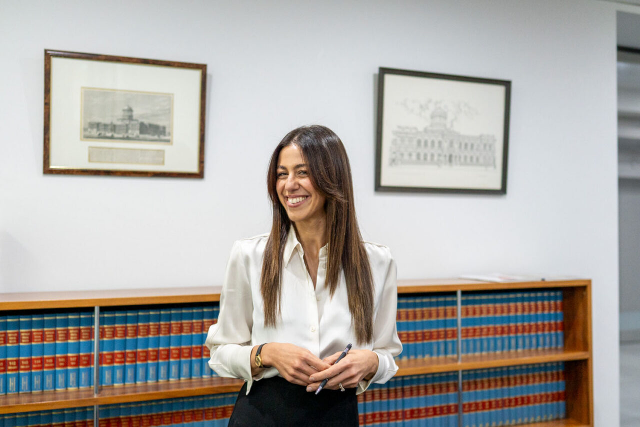 Female lawyer standing in front of a wall of law books smiling in a Melbourne legal office, framed architectural prints on the wall above