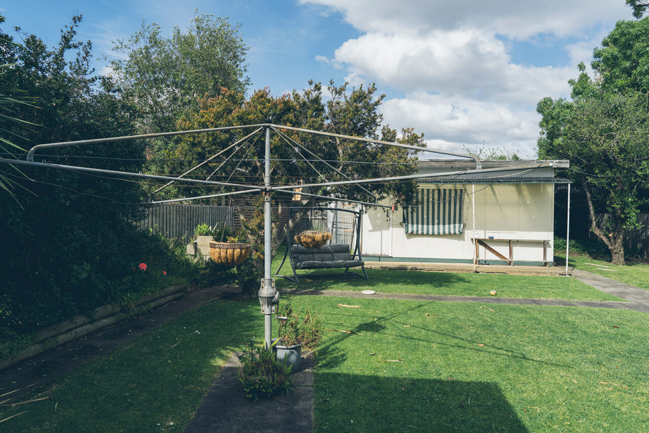 Family home backyard with a Hills Hoist clothesline, garden swing seat and lawn, documentary photography Melbourne