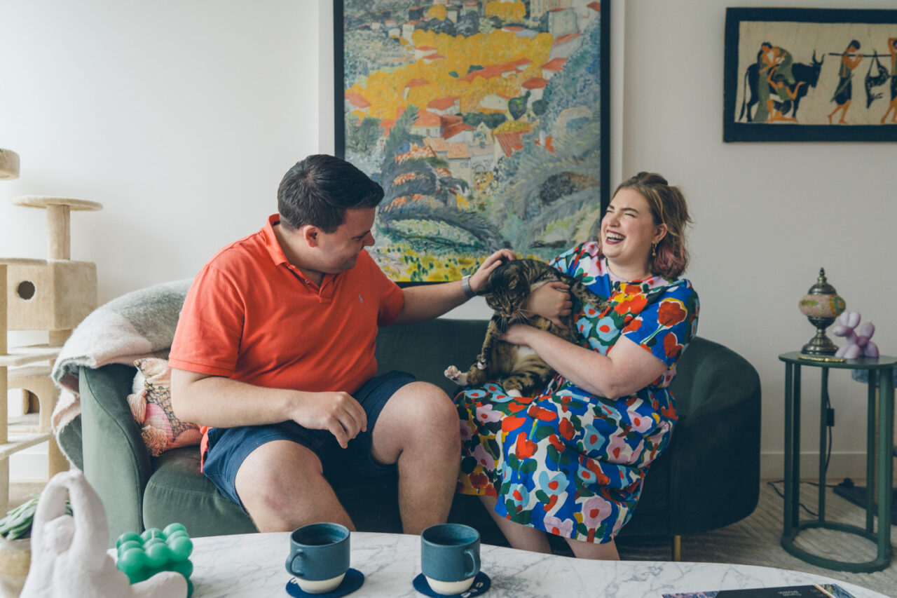 Couple sitting on a couch laughing together with their cat, documentary family home photography Melbourne