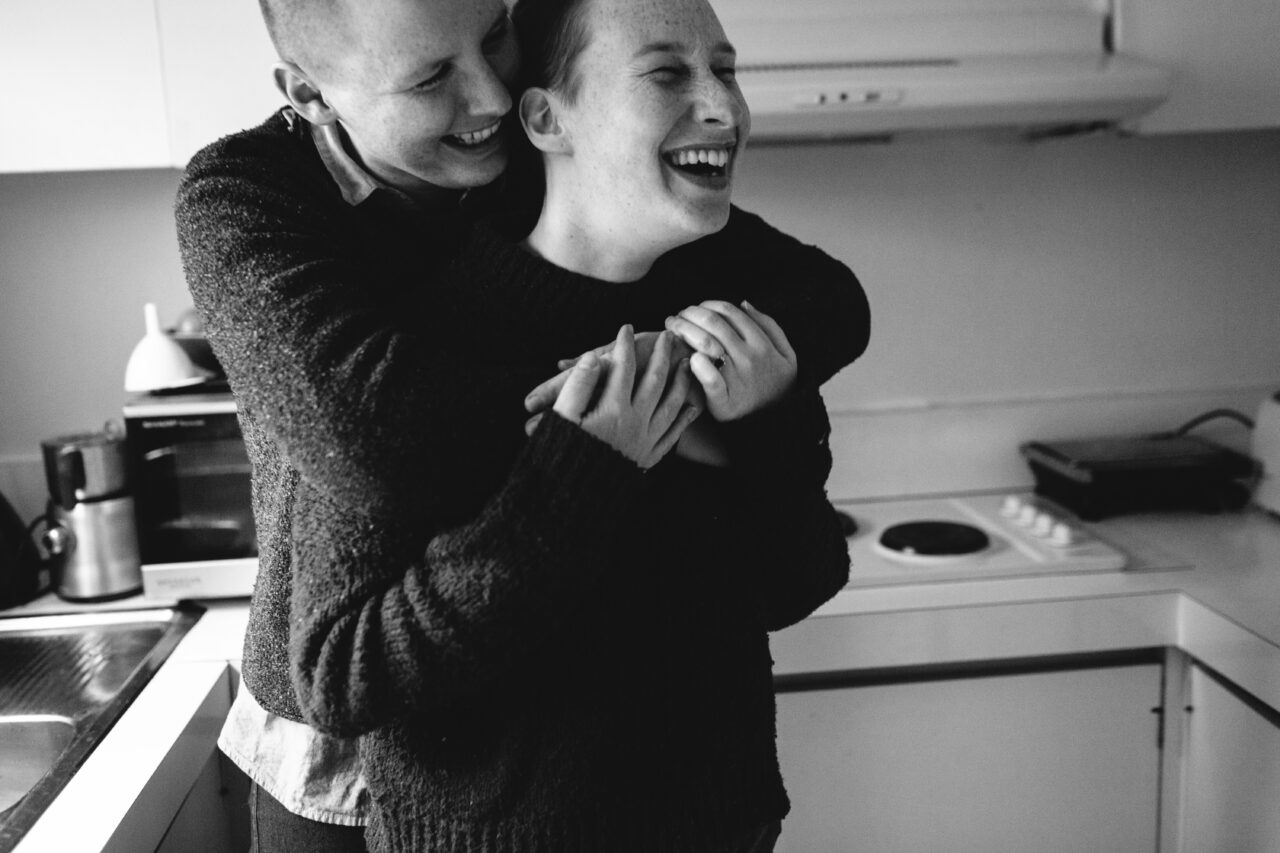 Couple embracing and laughing together in their kitchen, black and white documentary family home photography Melbourne