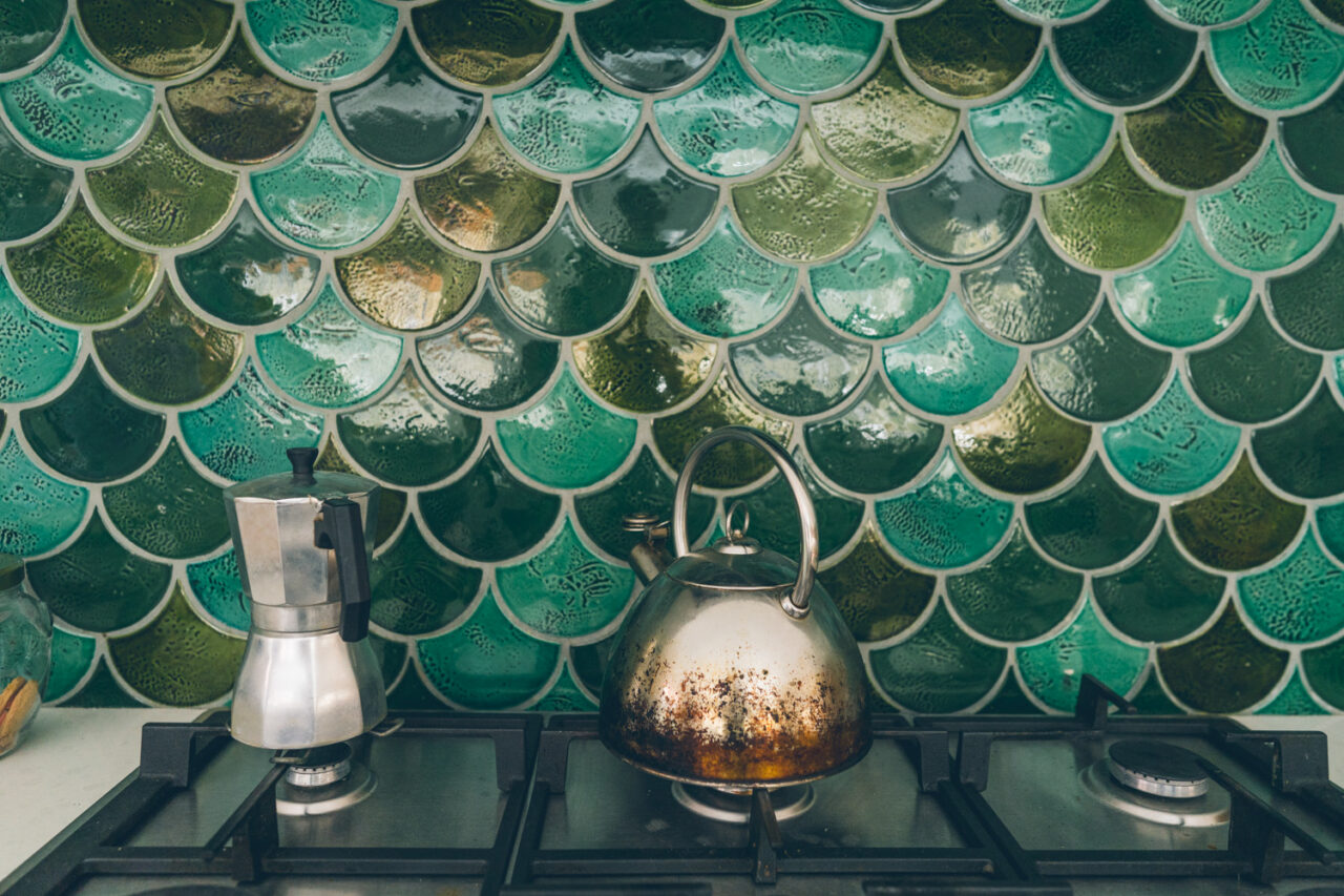 Distinctive green scale kitchen tiles with moka pot and kettle on a gas stove, documentary family home photography