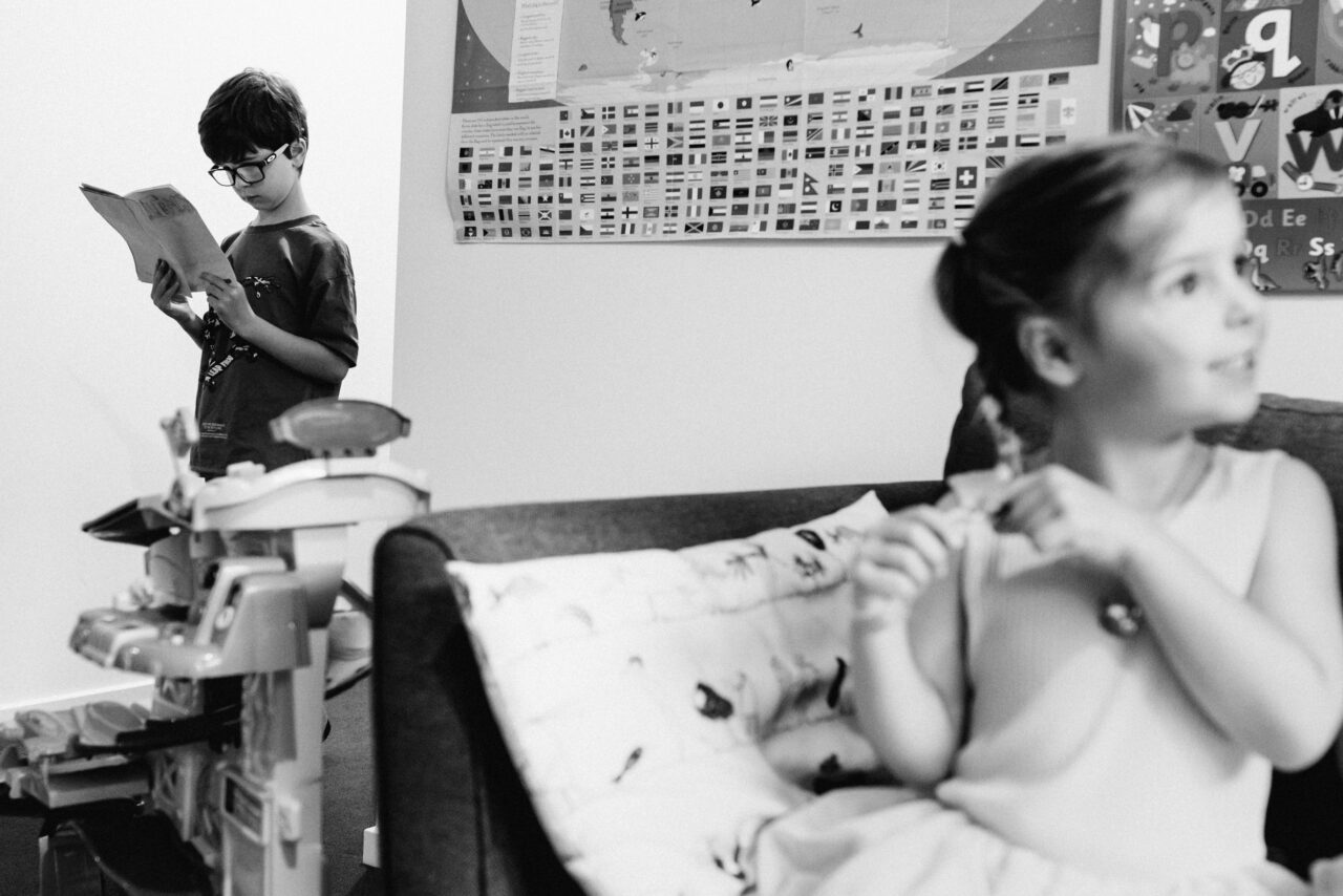 Two siblings occupying their own separate worlds in the same room, one reading and one daydreaming, black and white documentary photography