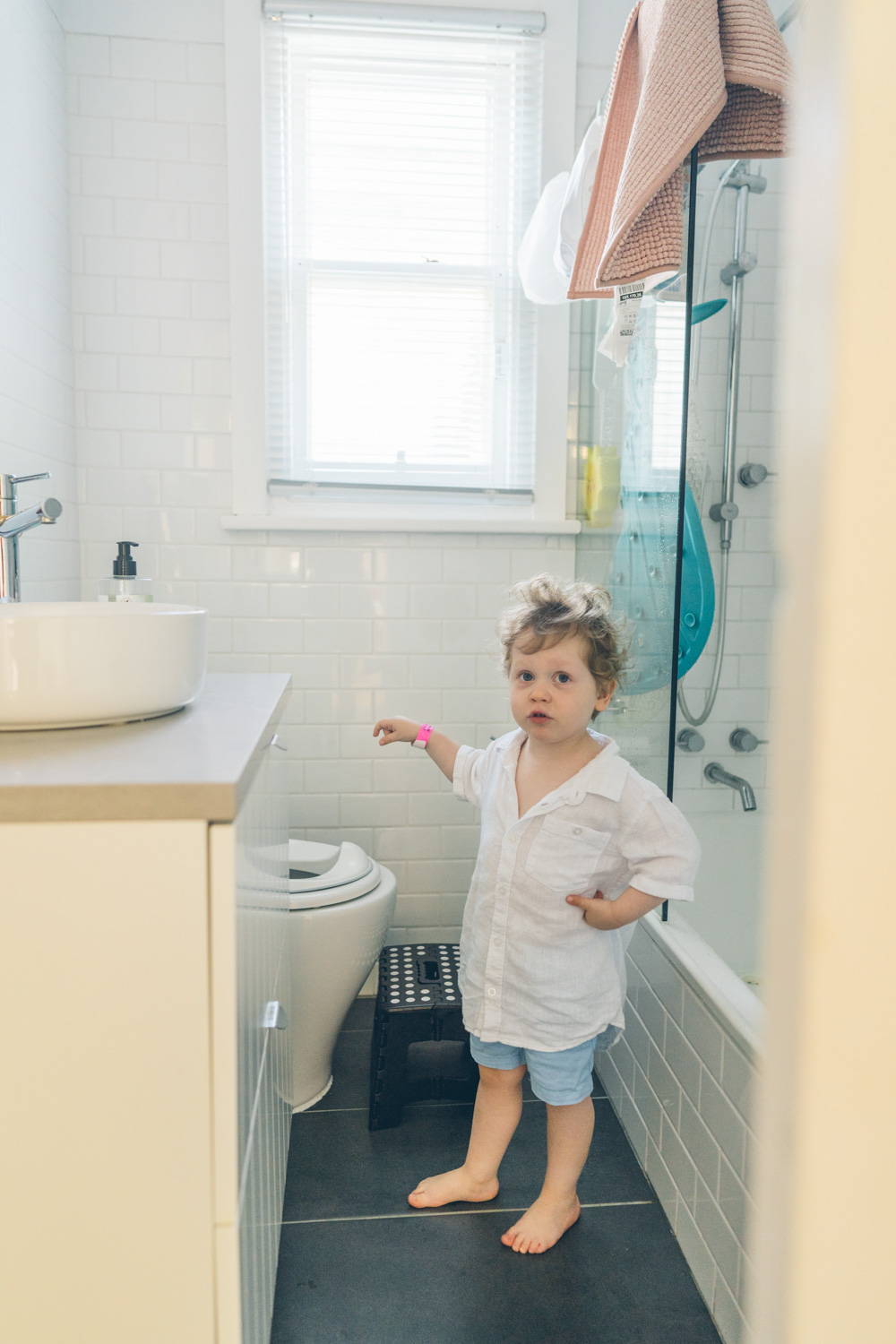 Toddler standing in a bathroom with the energy of someone who has made a decision, documentary family home photography