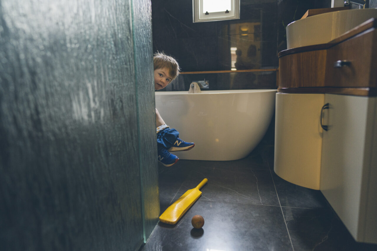 Childs head popping out from the wall with a cricket bat on the floor in a photography shoot in Melbourne