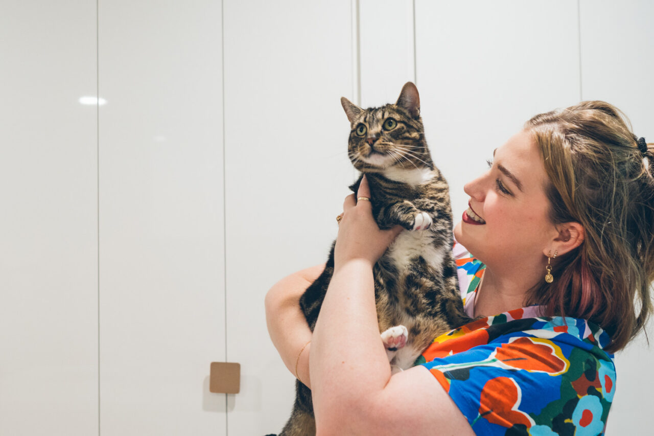 Woman holding up a tabby cat and laughing in her home, documentary family home photography Melbourne