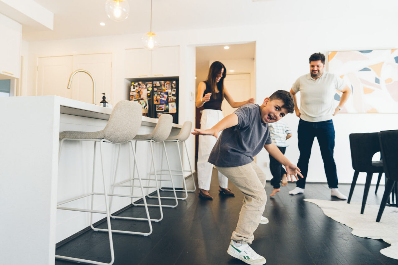oung boy mid-dance move in the kitchen during an in-home documentary family session in Melbourne, parents laughing in the background