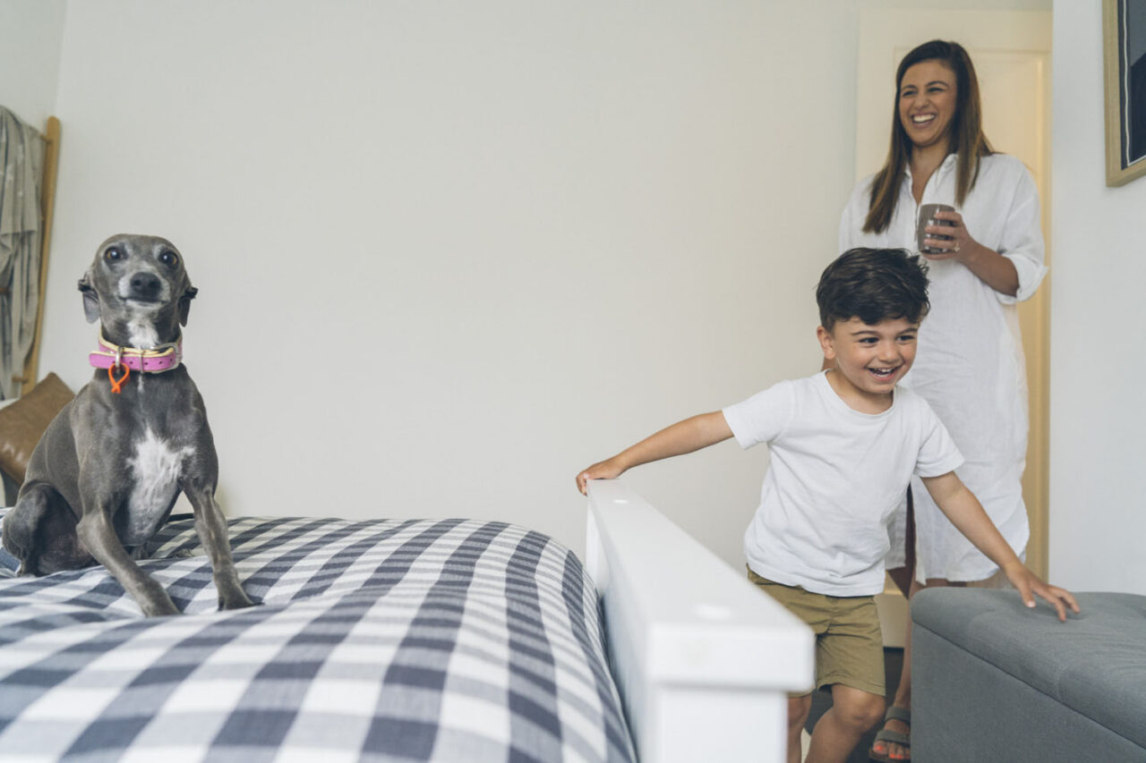 oung boy climbing on the bed next to an Italian greyhound while his mother stands in the doorway laughing during an in-home documentary family session in Melbourne