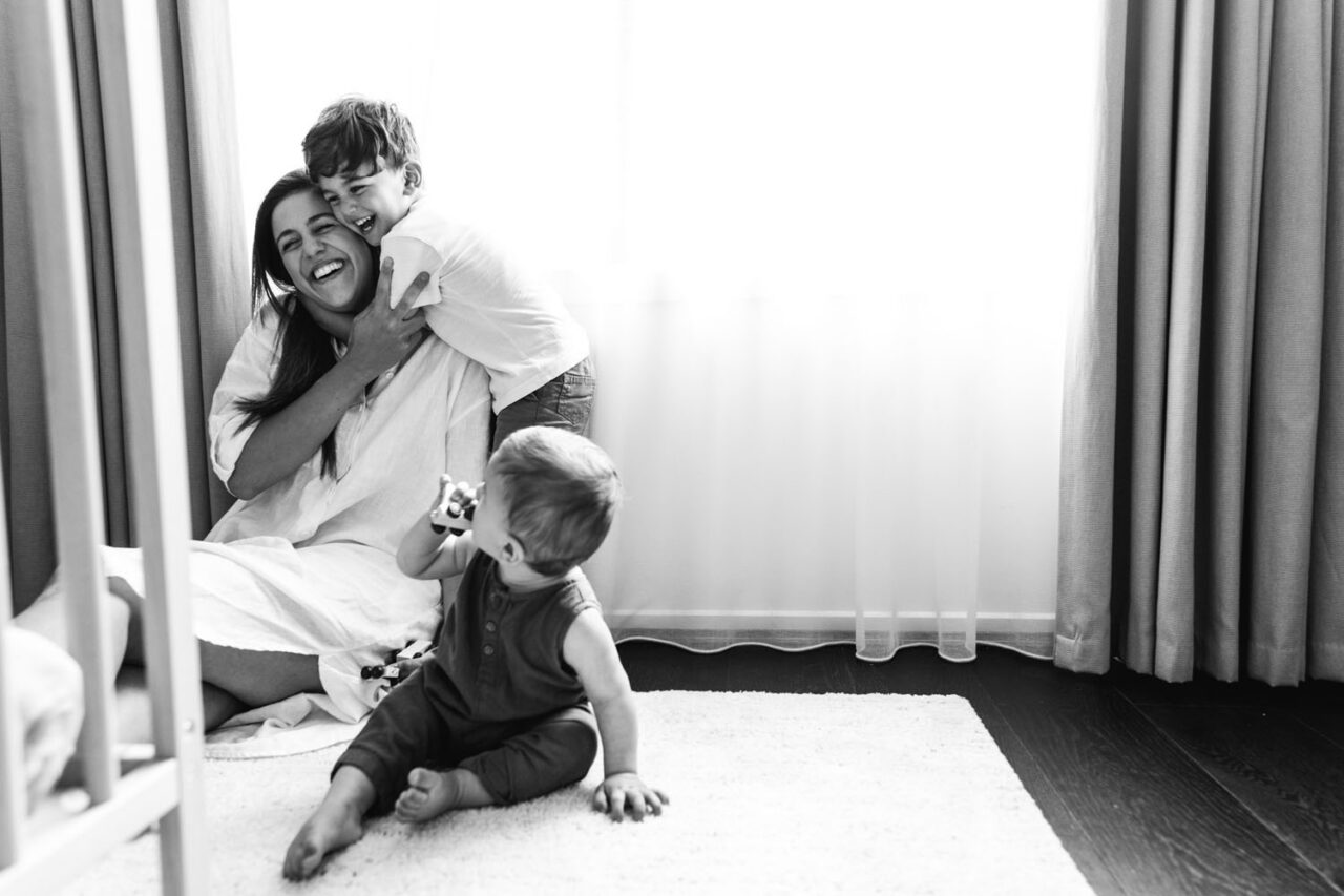 other sitting on the floor being hugged by her toddler son while baby plays nearby during an in-home documentary family photography session in Melbourne