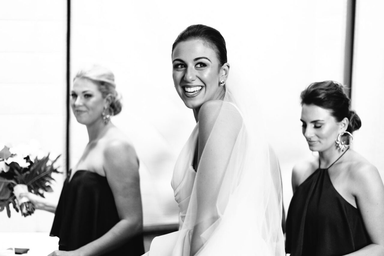 Bride laughing over her shoulder surrounded by bridesmaids in black during wedding preparations at Luminare South Melbourne