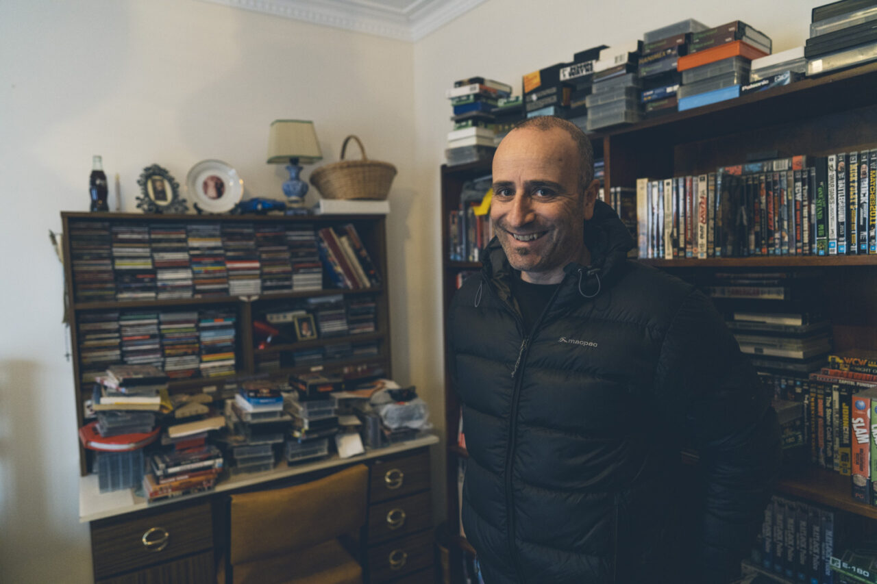 amily member smiling in front of shelves full of CDs, DVDs and VHS tapes during a deceased estate photography session in Melbourne